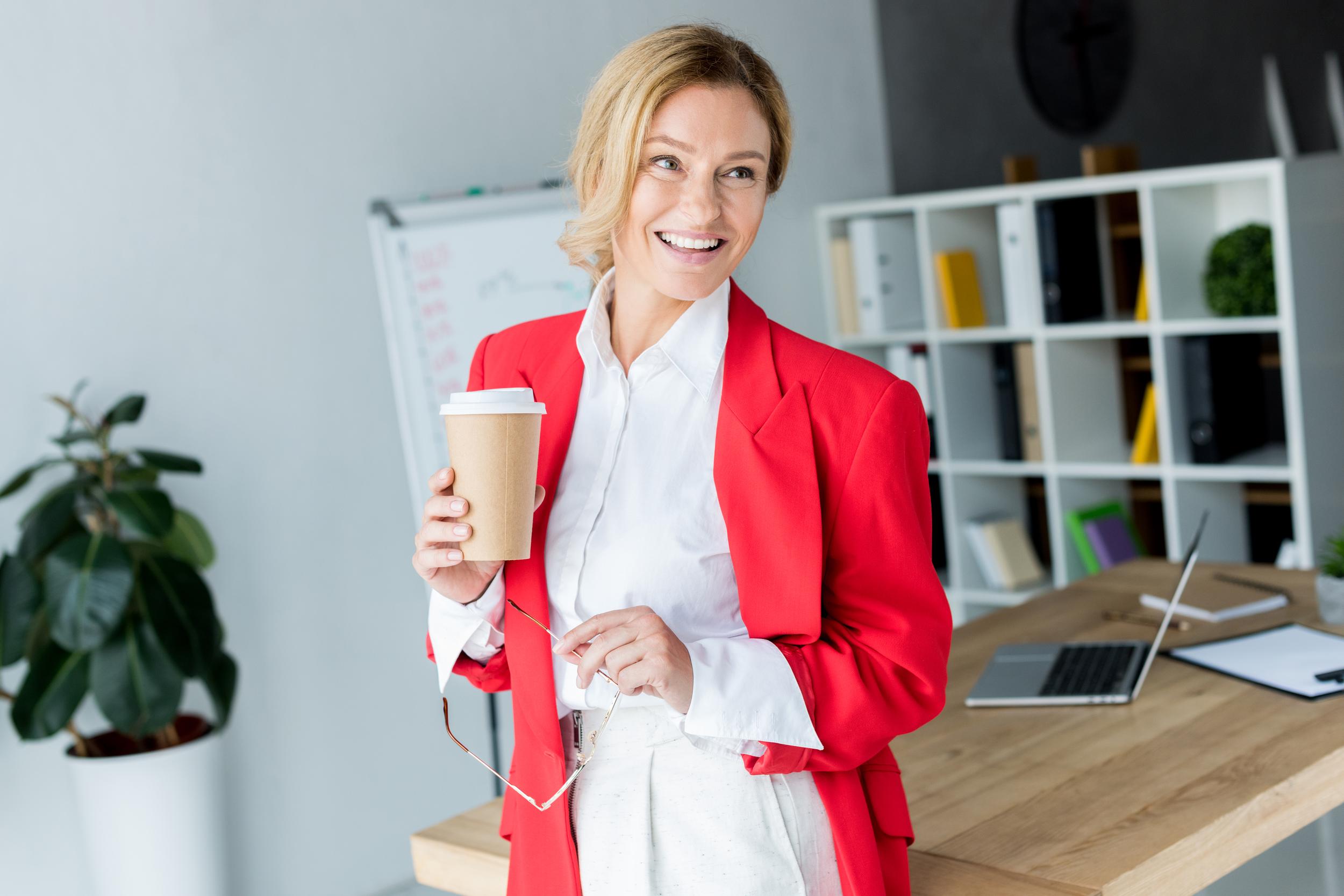 attractive businesswoman standing with coffee in paper cup in office